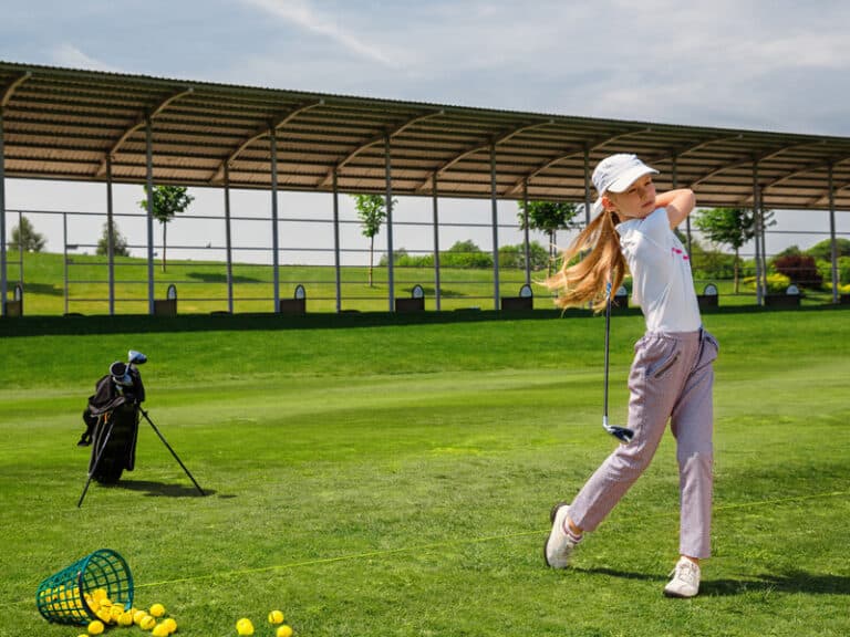 Young girl golfer on the driving range hitting golf balls.
