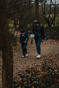 A young junior golfer walks along a wooden path with his dad who is carrying his golf bag.